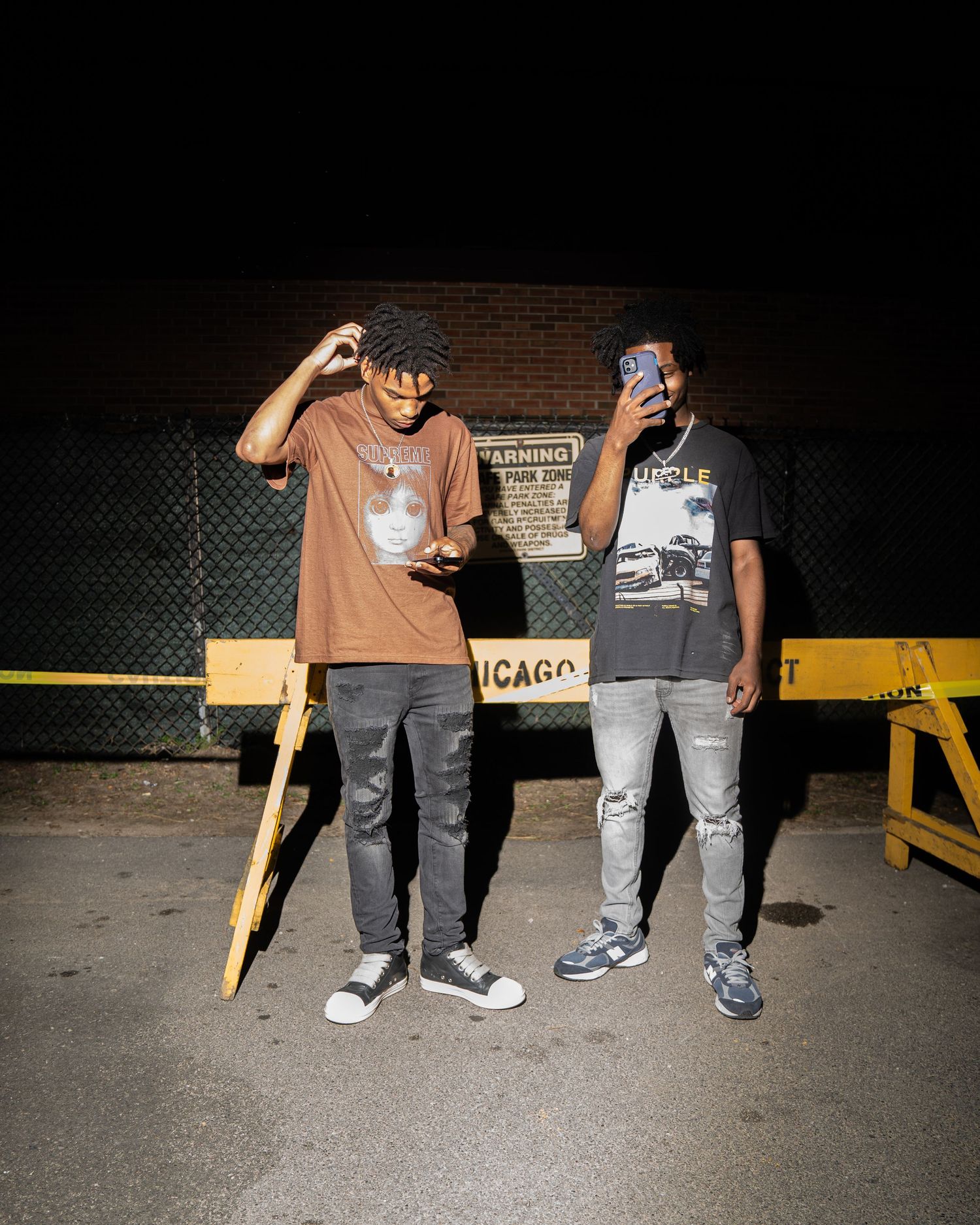 Two people in casual wear posing at night against brick wall with Chicago sign.