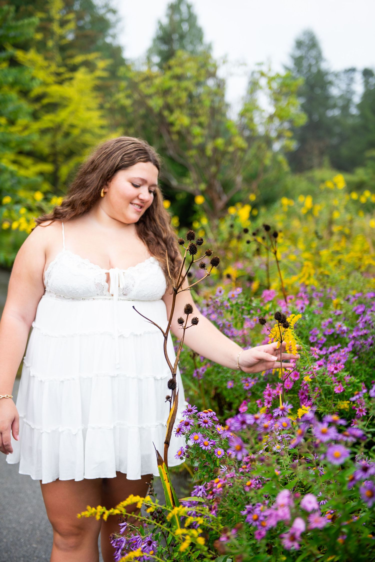 Senior portrait in white dress posing among colorful wildflowers and purple blooms.