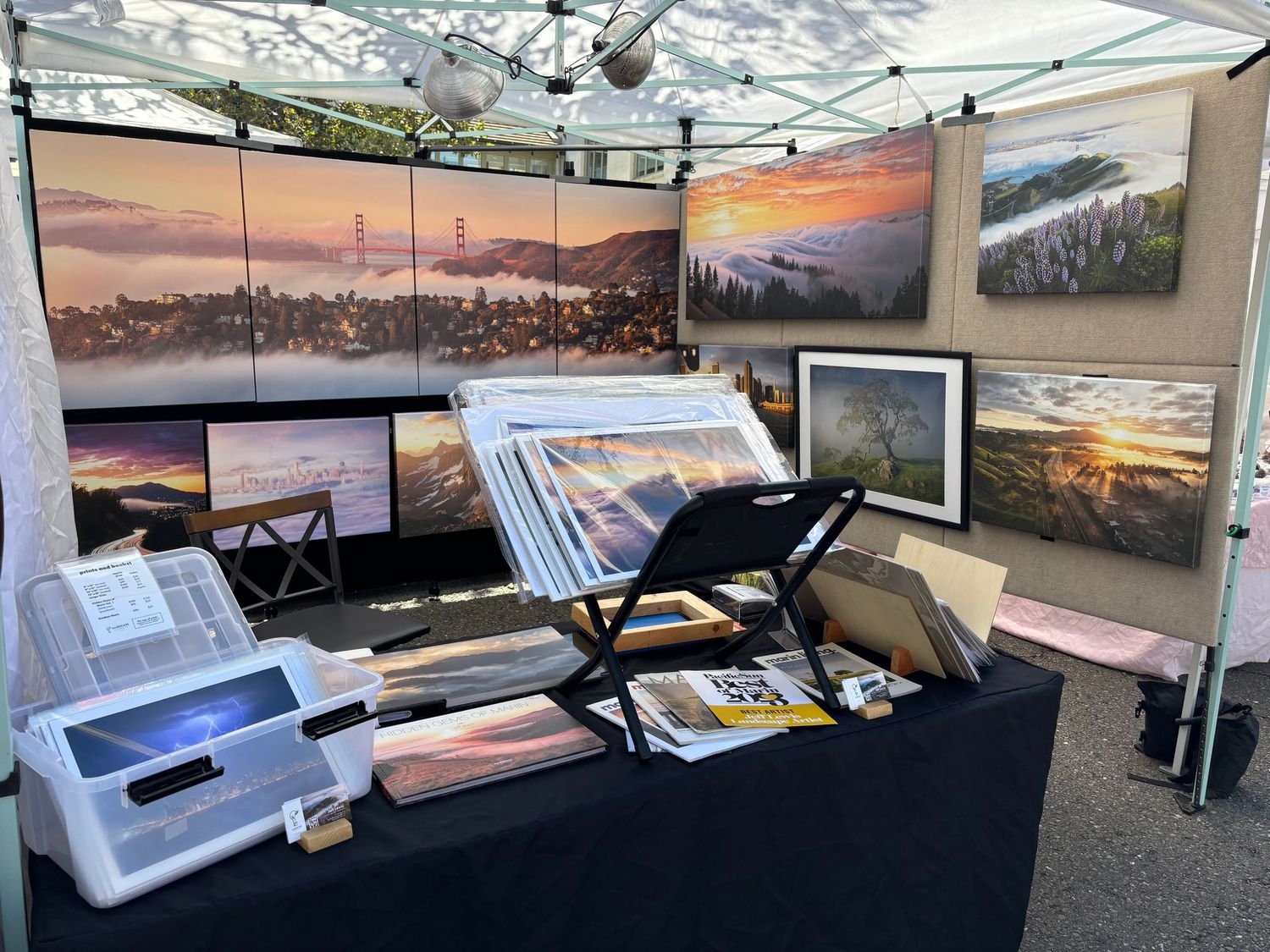 Art vendor booth displaying sunset landscape photographs and prints under a white canopy.