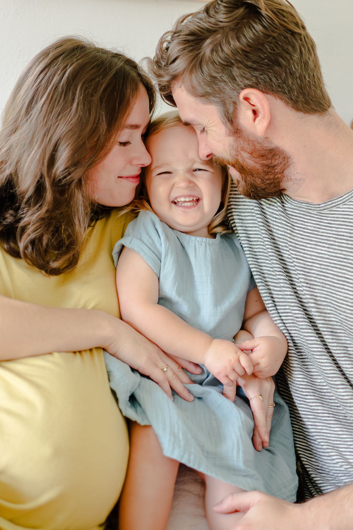 Mom and dad snuggling close to their little girl, creates a nose-scrunch smile that radiates joy!