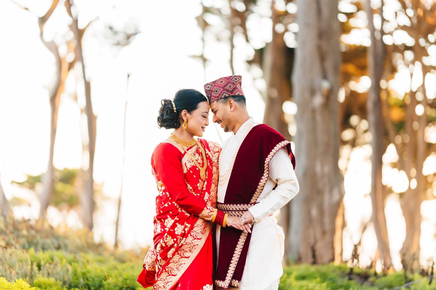 Newlyweds in red and white traditional Nepali dress share an intimate moment at sunset.
