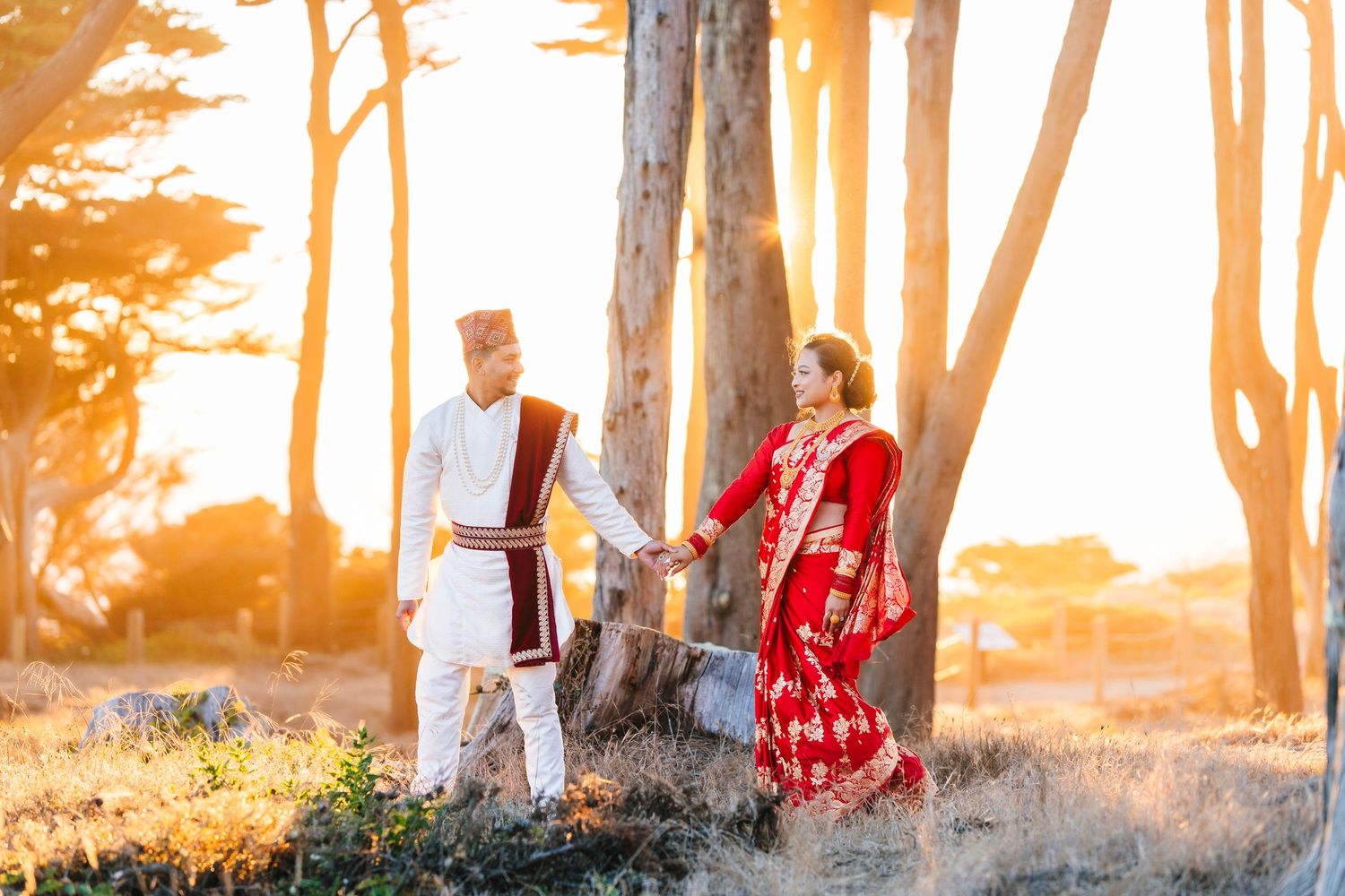 A couple in traditional Nepali wedding attire poses in a forest during golden hour.