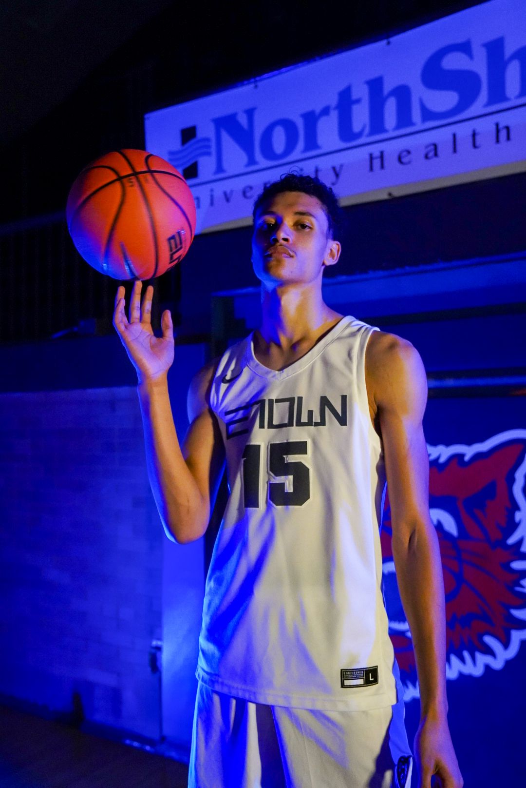 Basketball player in white jersey posing with ball under blue lighting and NorthShift banner.
