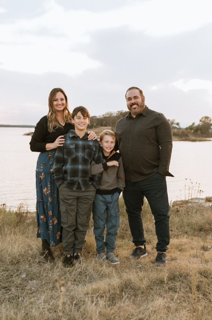 Family group posing together on hillside with water and cloudy sky in background.