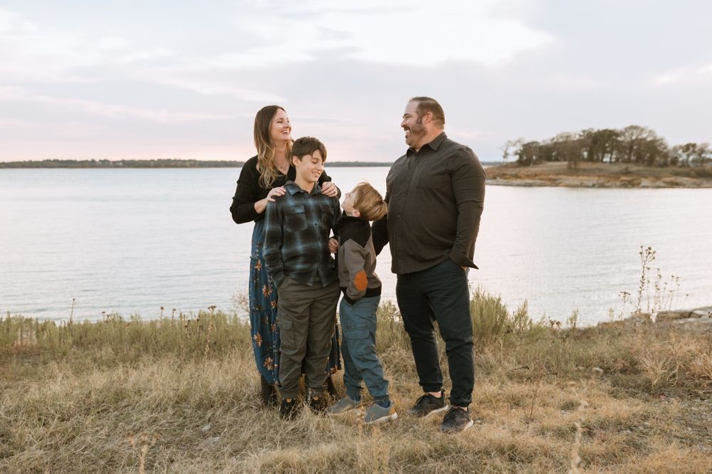 Family members sit together on grass overlooking a scenic waterfront landscape.