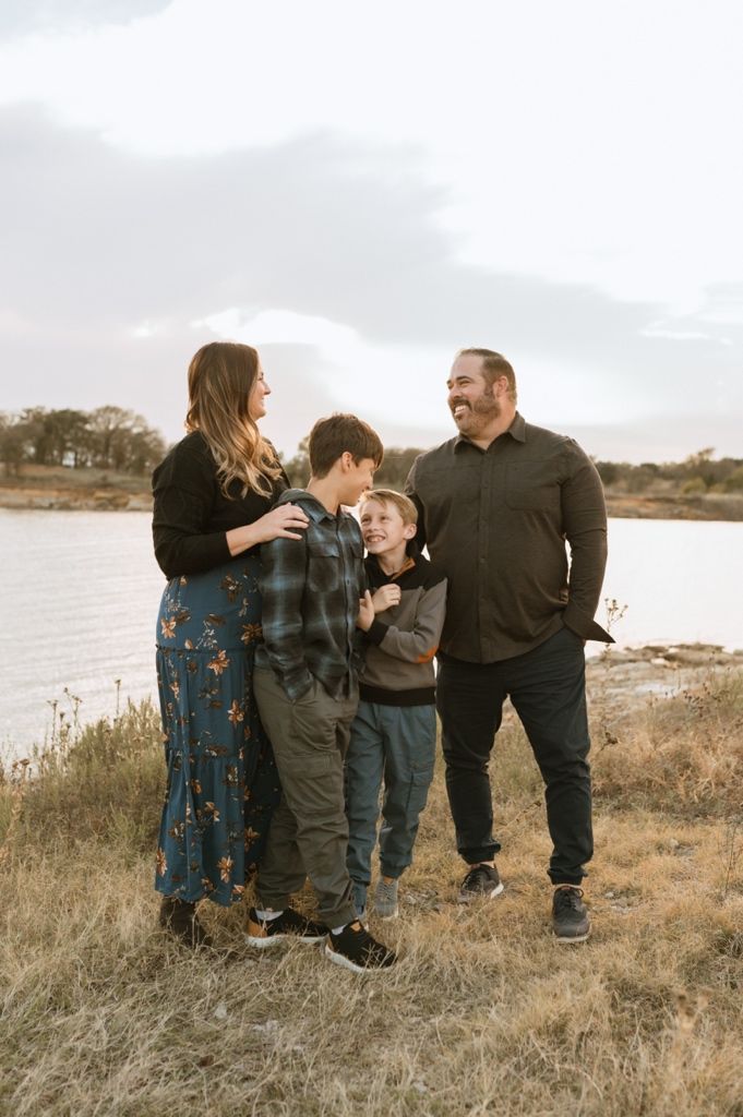 Family enjoying a candid moment together on a grassy hillside overlooking a lake at sunset.
