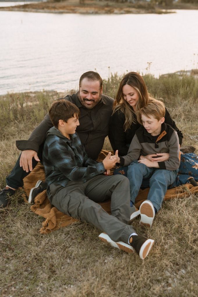 Family relaxing together on grass while looking at their mobile phones on a cloudy day.