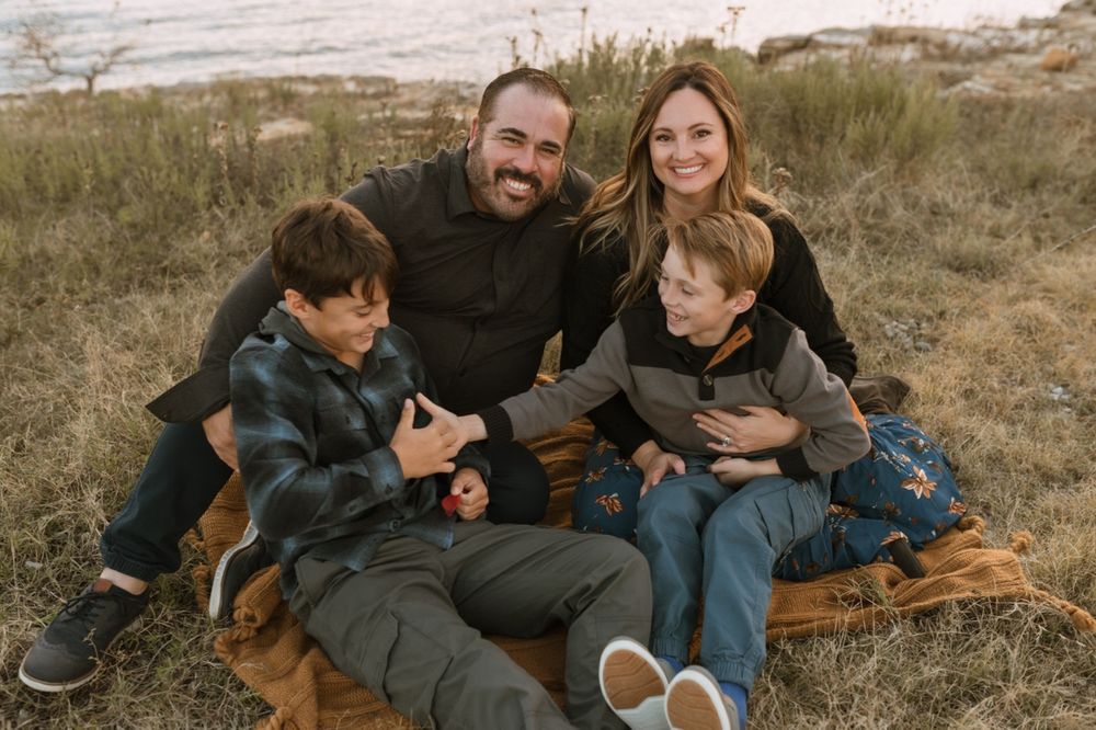 Family and dog relaxing together on grassy field during golden hour outdoor photo session.