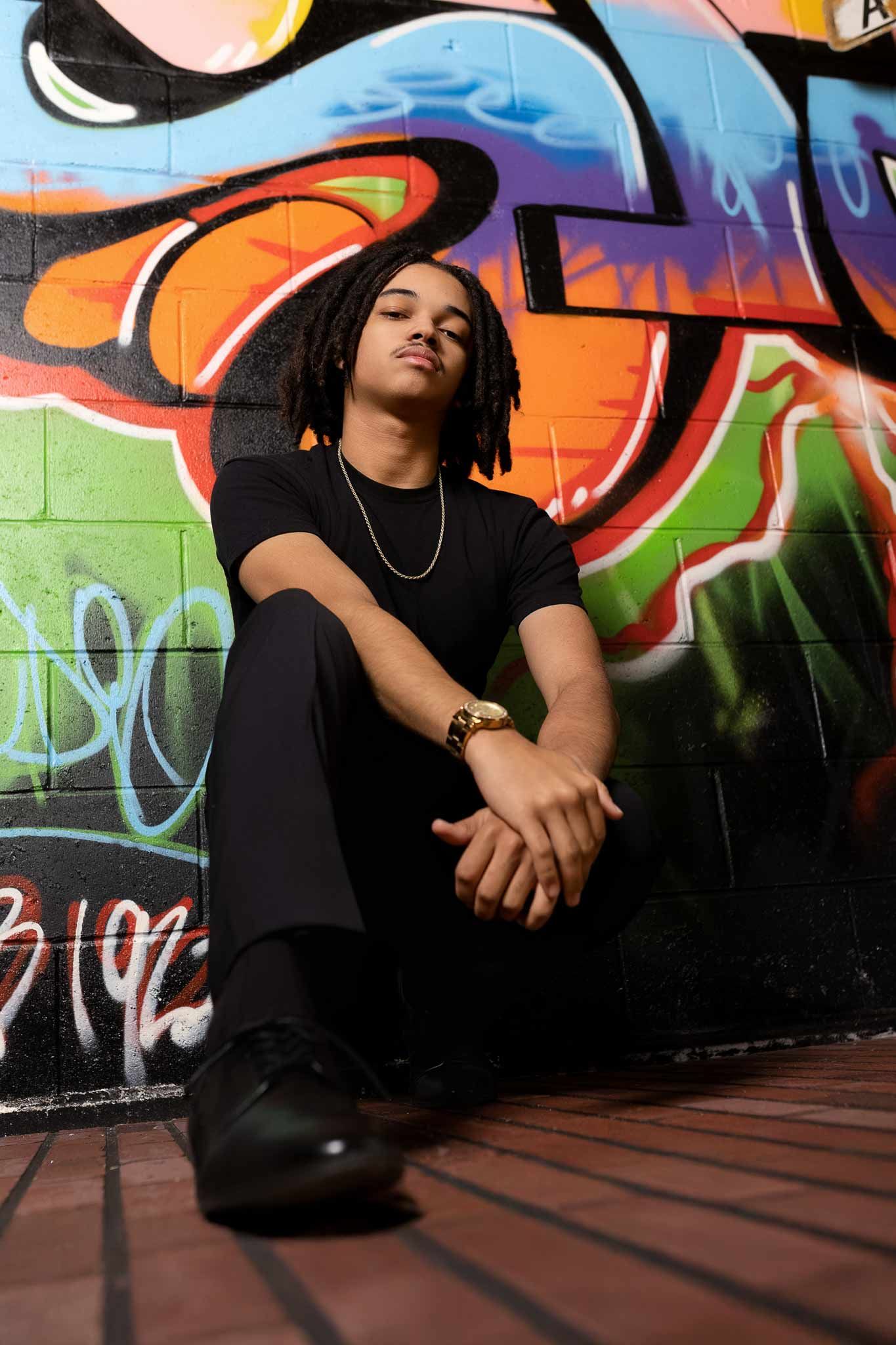 Urban portrait against vibrant graffiti wall with colorful swirling designs in orange, blue and black.