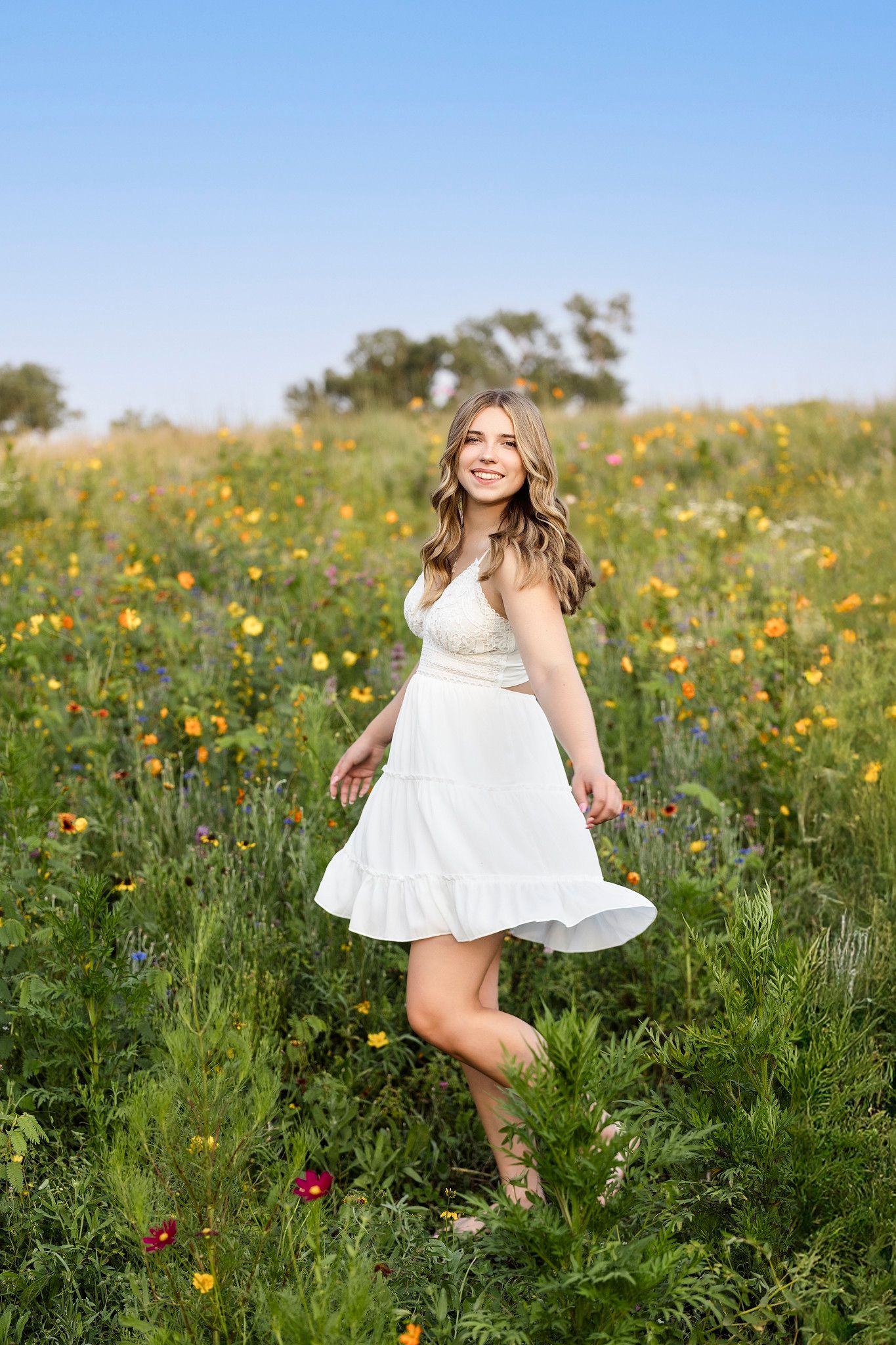 A person in a white dress twirls and dances joyfully through a vibrant wildflower meadow on a sunny day.