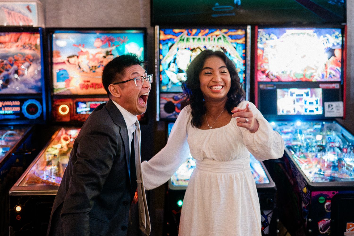 Couple celebrating at a pinball arcade with colorful neon lights and classic arcade games in the background.