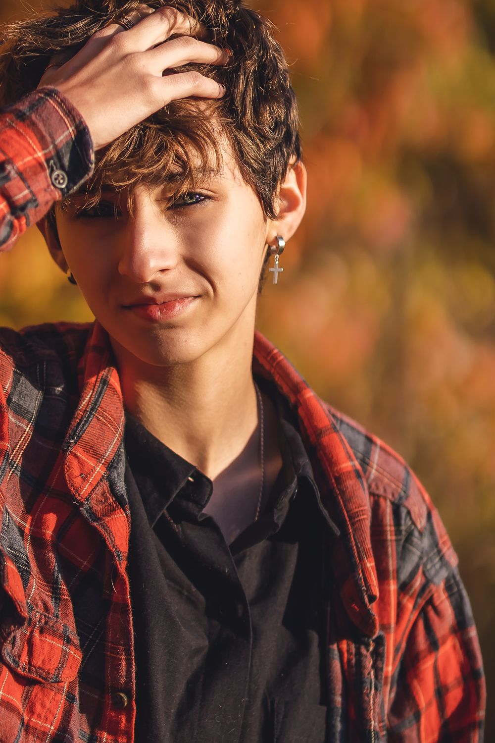 Person wearing red plaid flannel and black shirt in front of fall foliage.
