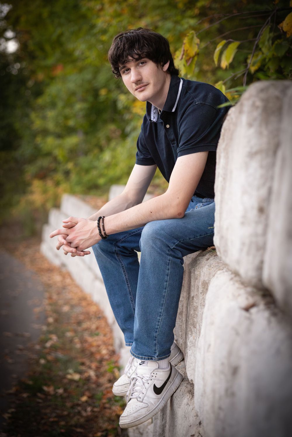 Person in casual wear sitting on a concrete wall with Nike sneakers in an outdoor setting.