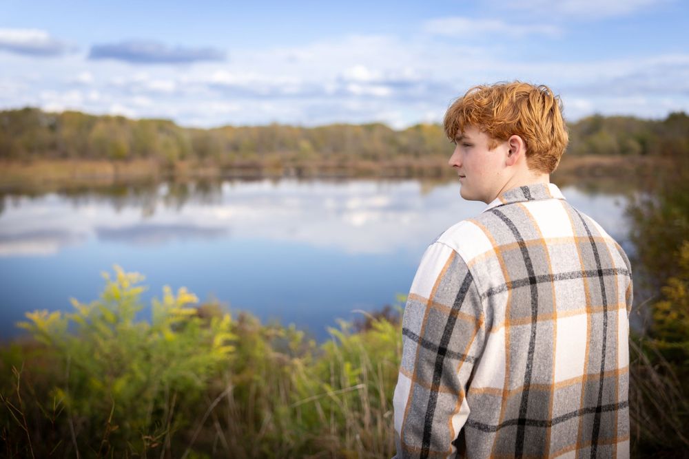 Person in plaid jacket gazes across serene lake landscape during golden hour.