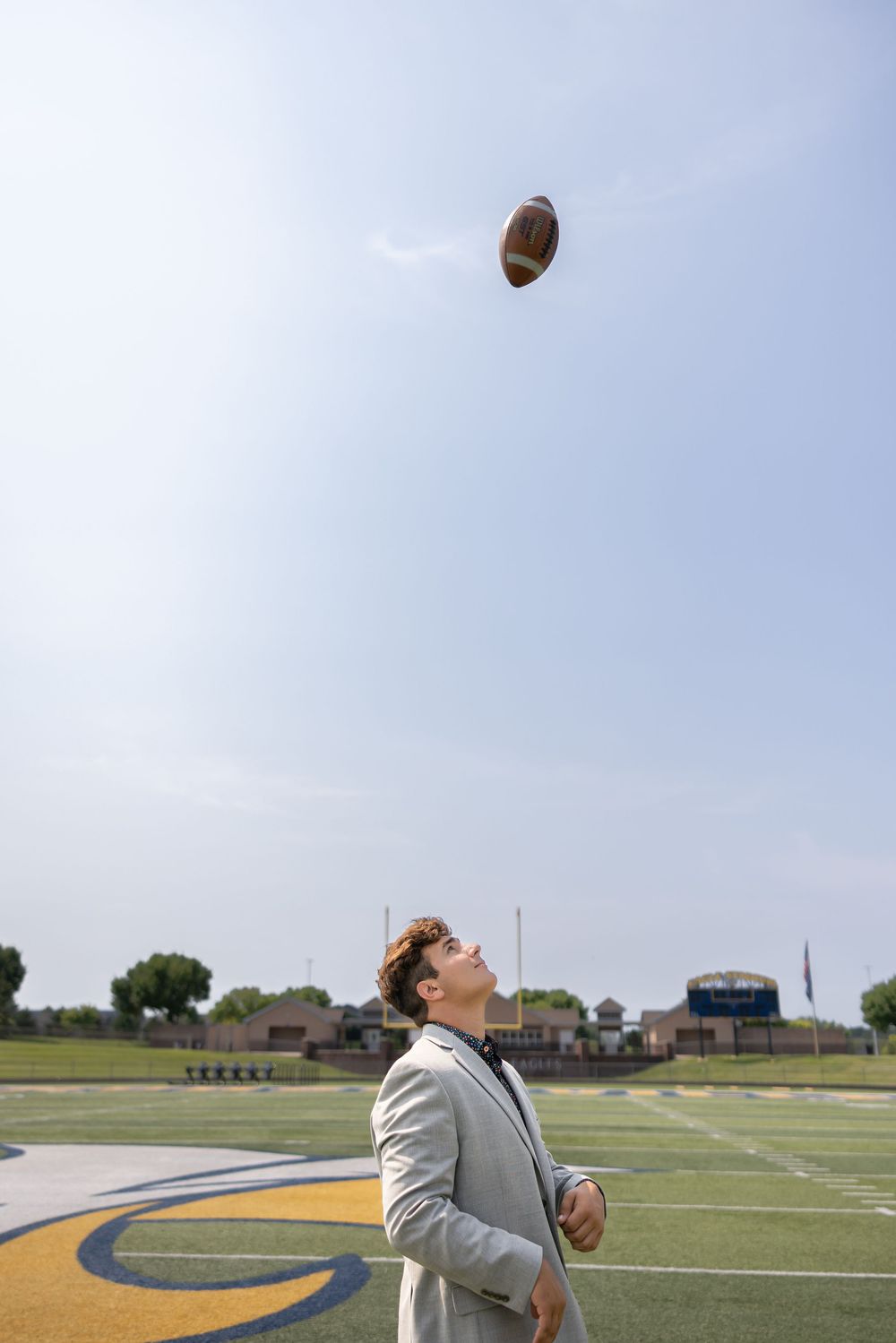 Football player looks up at ball falling from sky during practice on sports field.