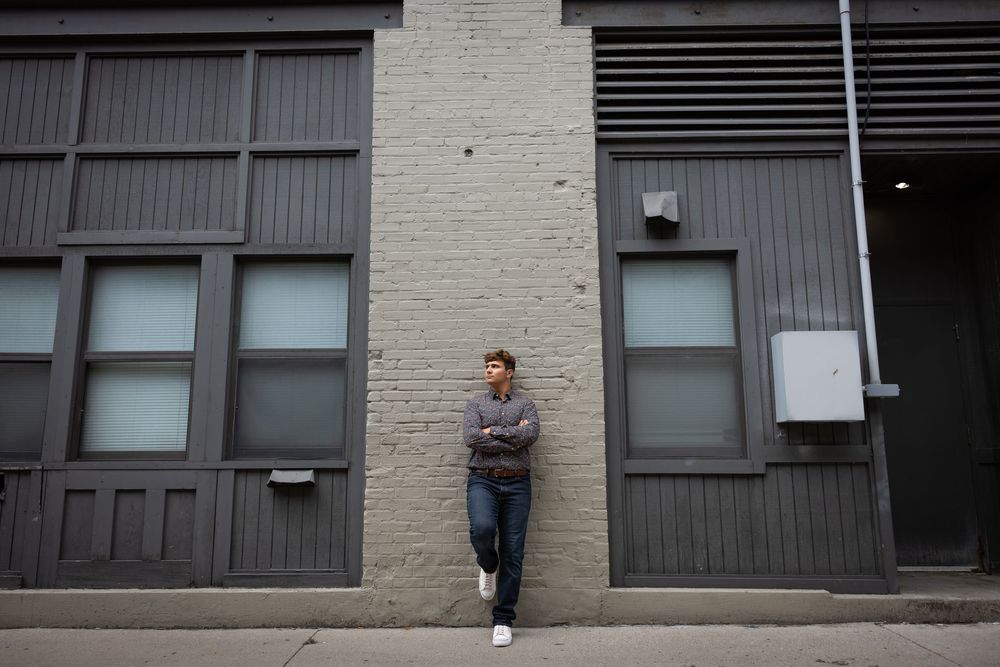 Person stands against industrial brick building facade with windows and metal vents.