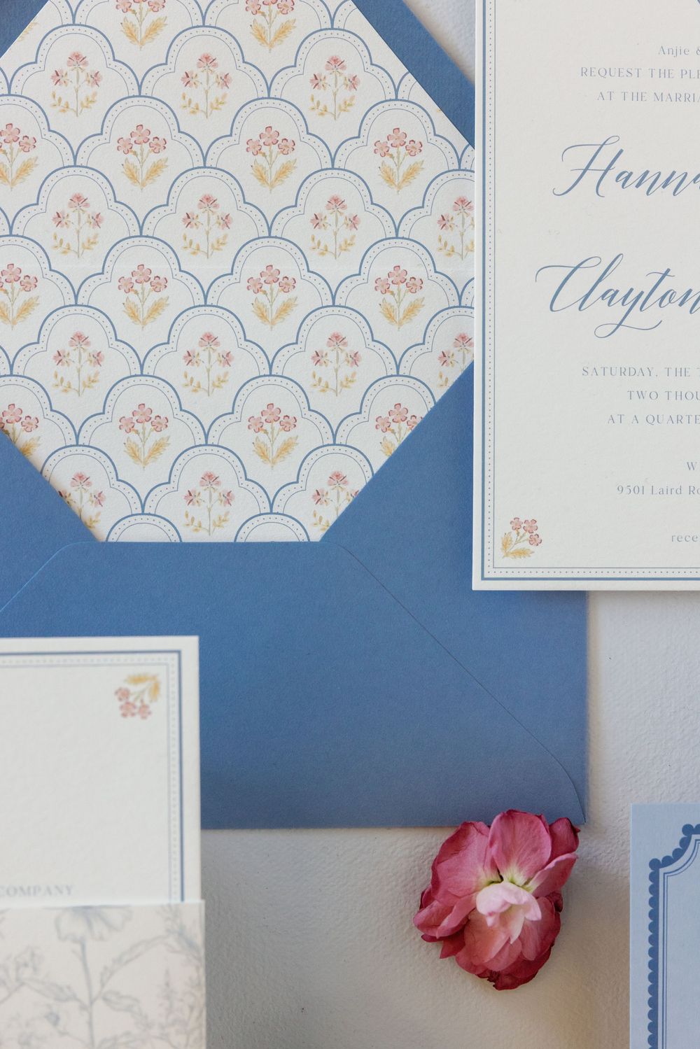 Wedding invitation suite featuring blue envelopes and delicate floral pattern with scalloped details.