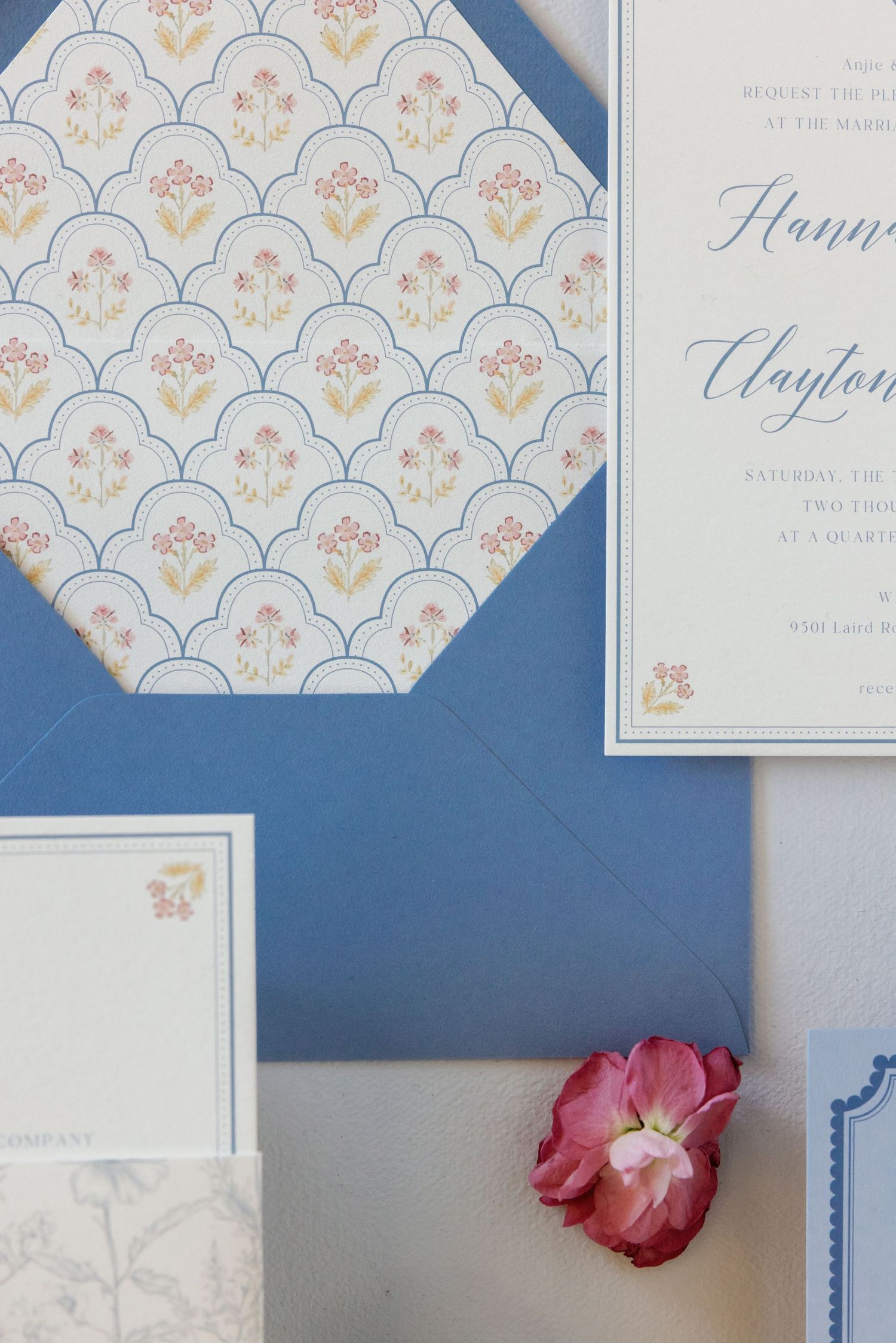 Wedding invitation suite featuring blue envelopes and delicate floral pattern with scalloped details.