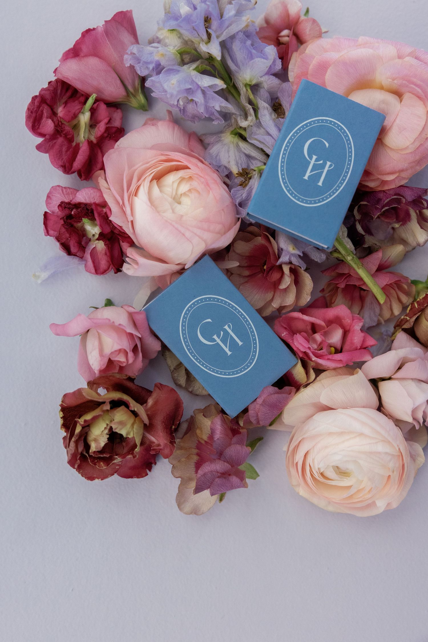 A delicate arrangement of pink and purple flowers with blue monogram cards on a light gray background.