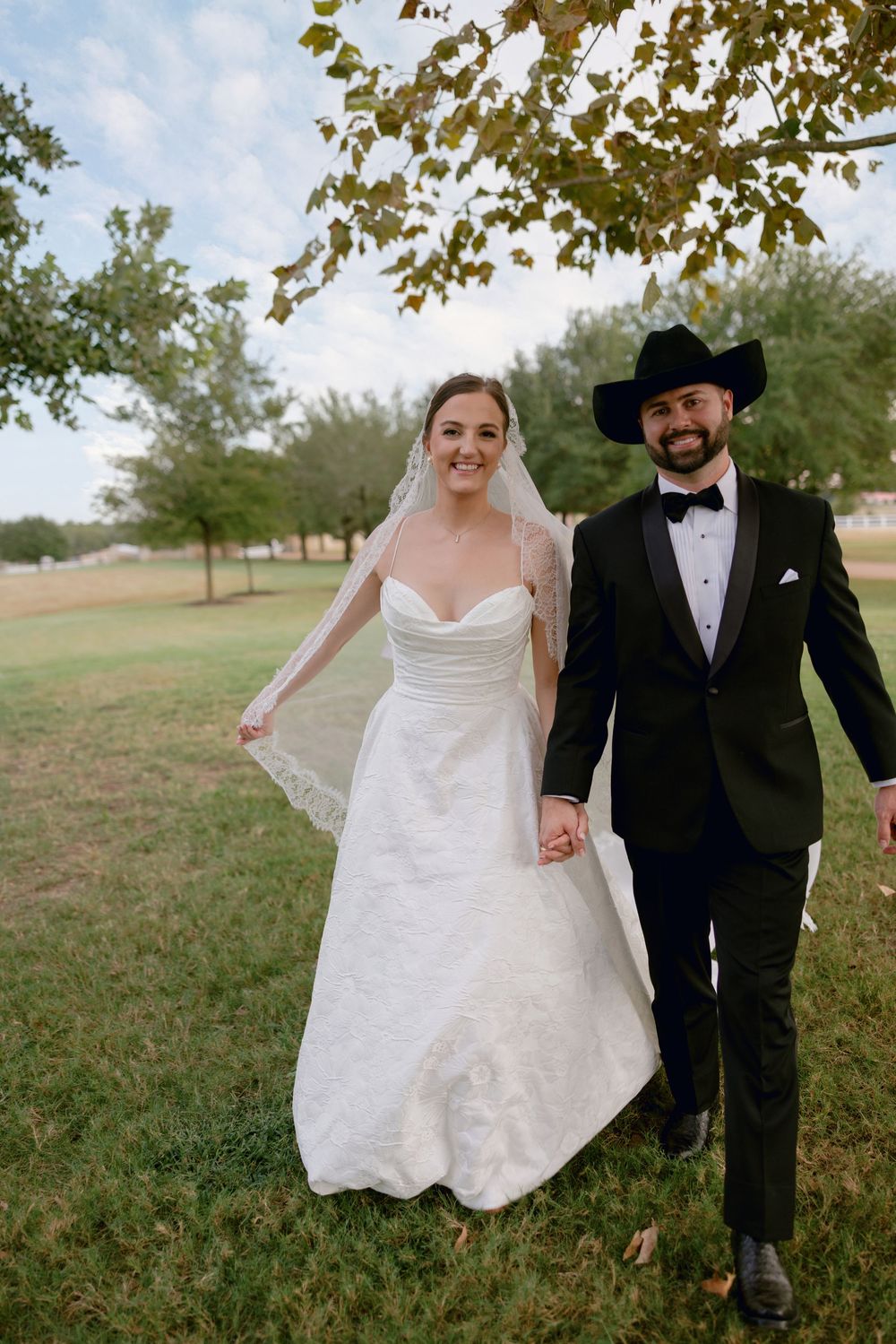 Couple walks and poses together outdoors, with bride in white dress and groom in black tuxedo.
