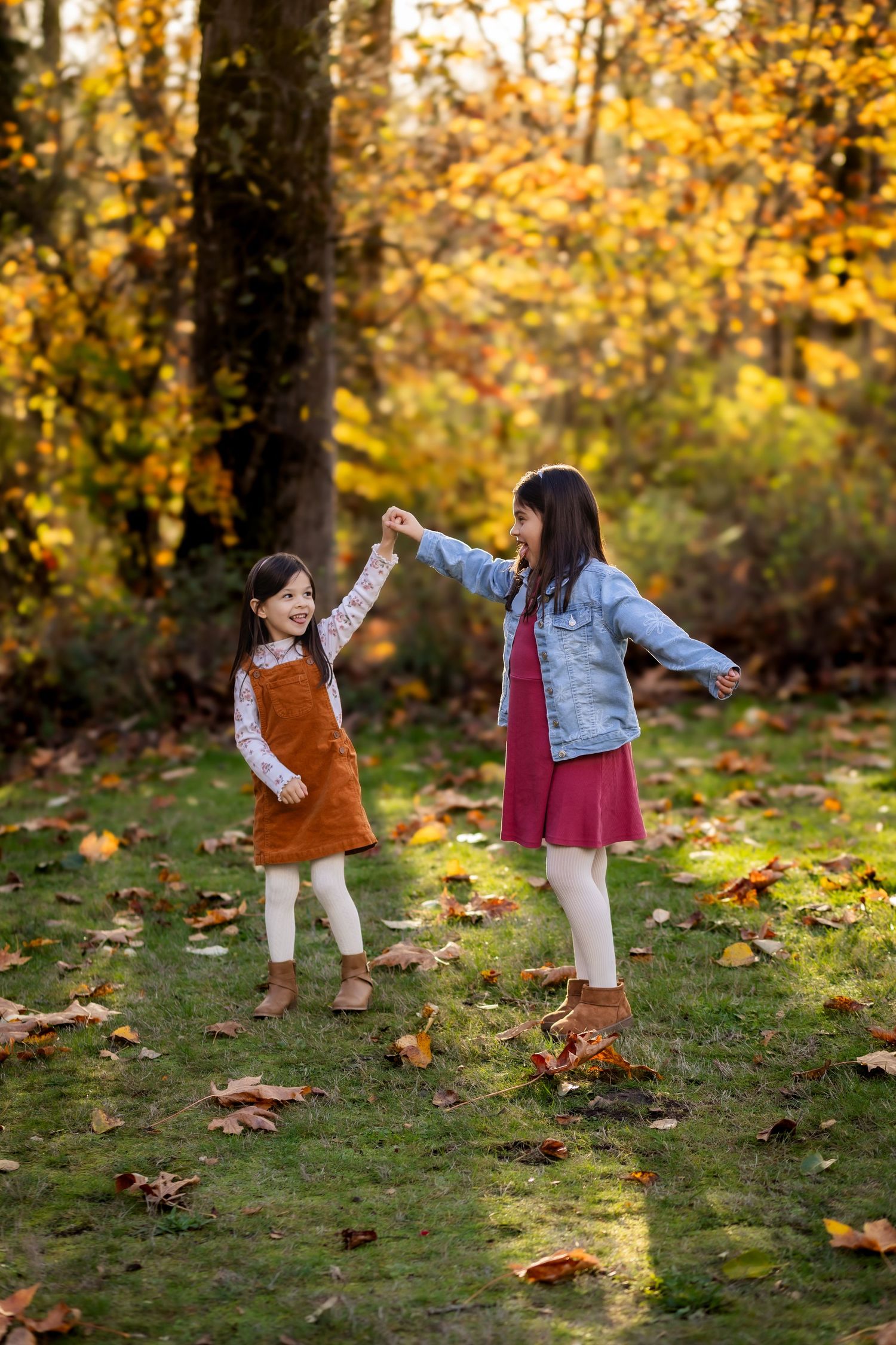 Two children playing together in autumn leaves during golden hour in a park setting.