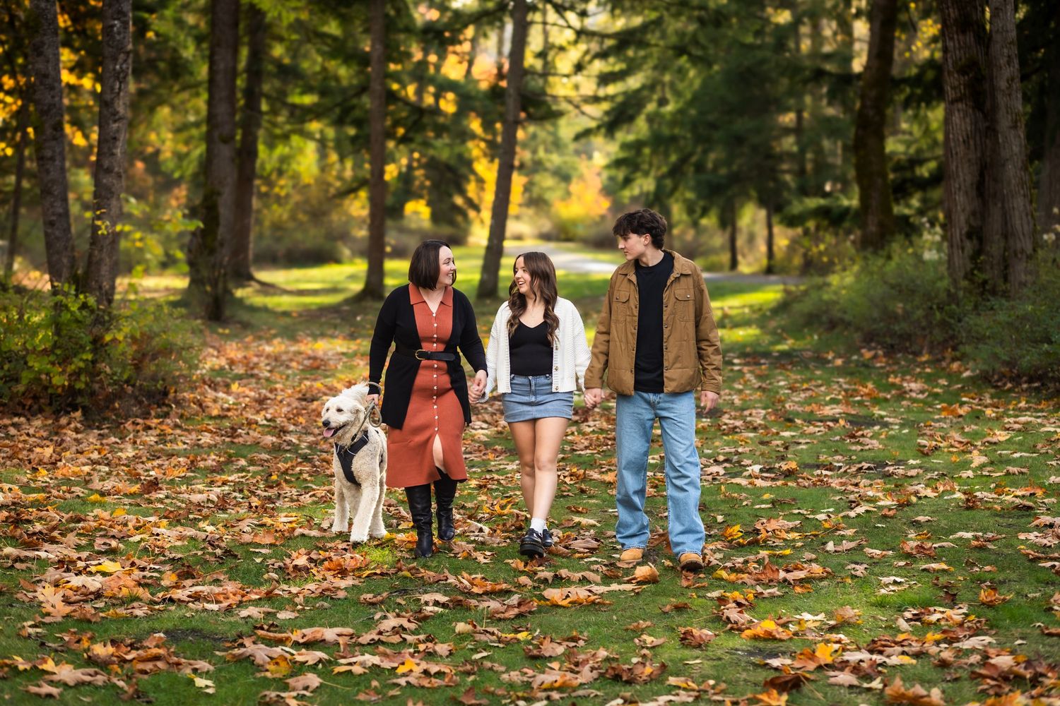 Family enjoying an autumn walk through a forest path covered in colorful fallen leaves during golden hour.