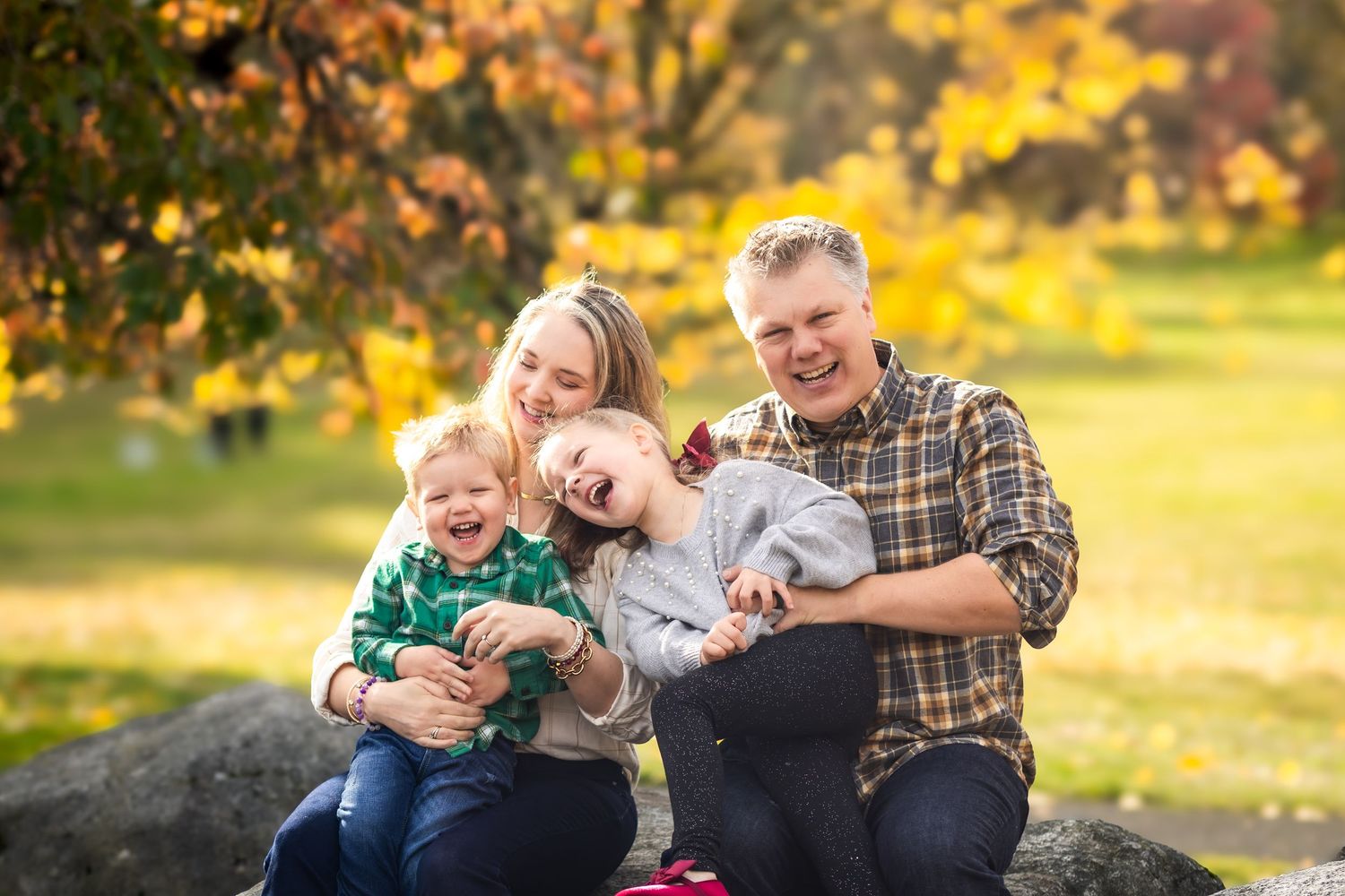 Family enjoying a playful autumn afternoon together in a park with golden fall foliage in the background.