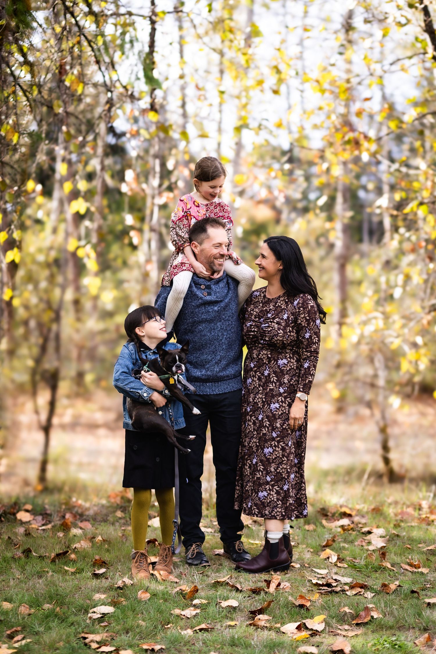 Family enjoying a playful autumn moment together in a wooded area with fallen leaves on the ground.