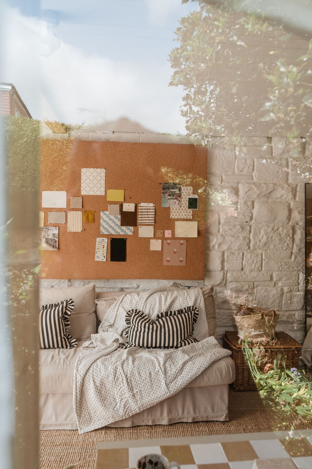 Cozy bedroom corner with striped pillows, neutral bedding, and cork board wall art display in warm natural lighting.