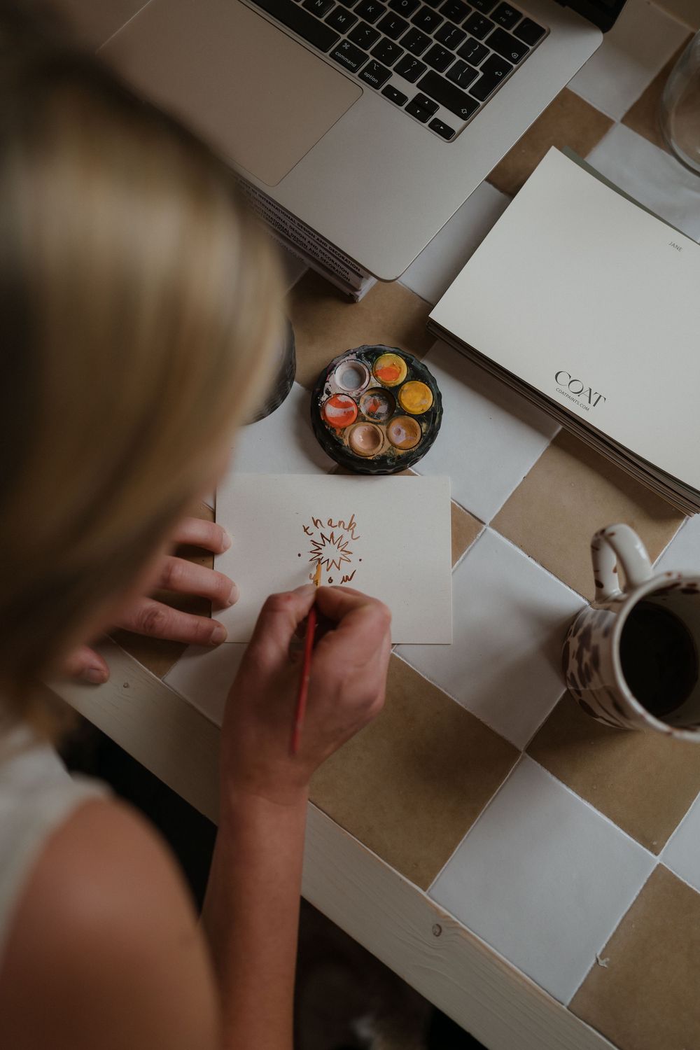 Top-down view of someone writing or drawing on white paper at a desk with a laptop keyboard visible in the frame.