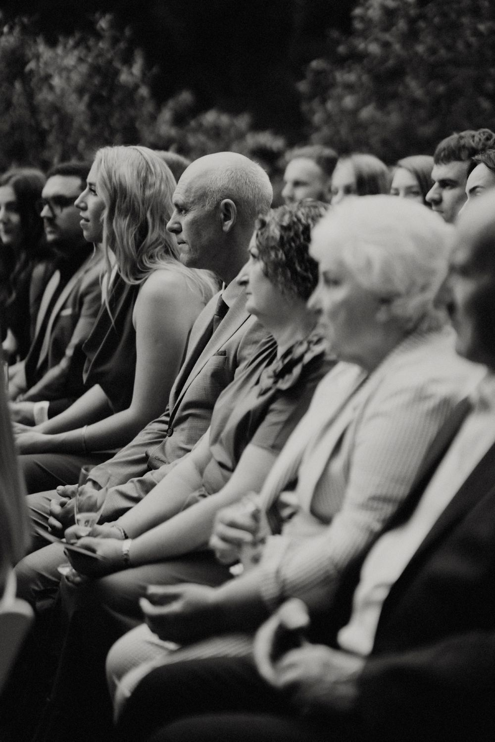 Black and white image of wedding guests seated in rows during an outdoor ceremony.