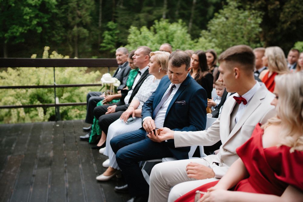 Wedding guests seated on wooden benches in an outdoor forest setting.