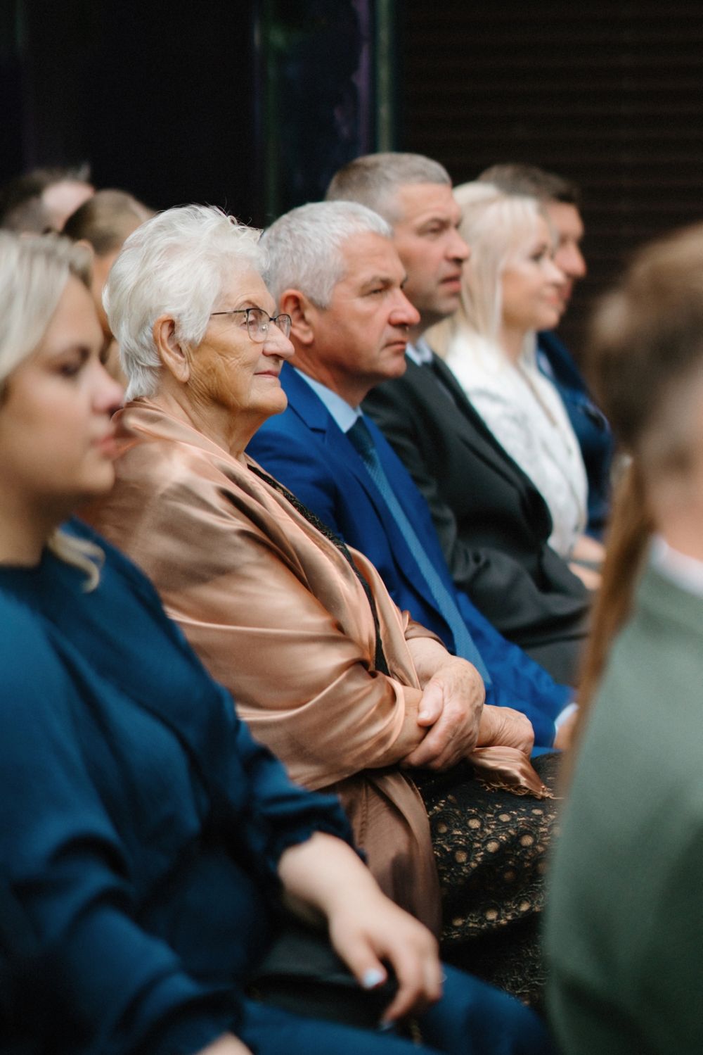 Wedding guests in formal attire seated during an outdoor ceremony.