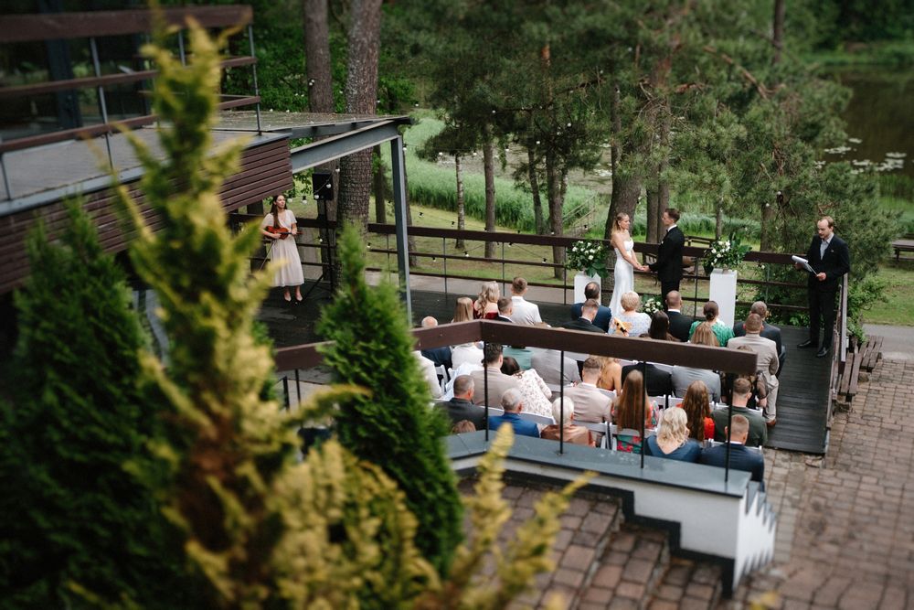 Wedding guests gather on a multi-level outdoor deck surrounded by pine trees during a celebration.