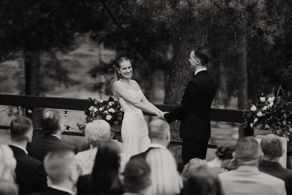 Black and white photo of an outdoor wedding ceremony with guests seated on a wooded hillside.