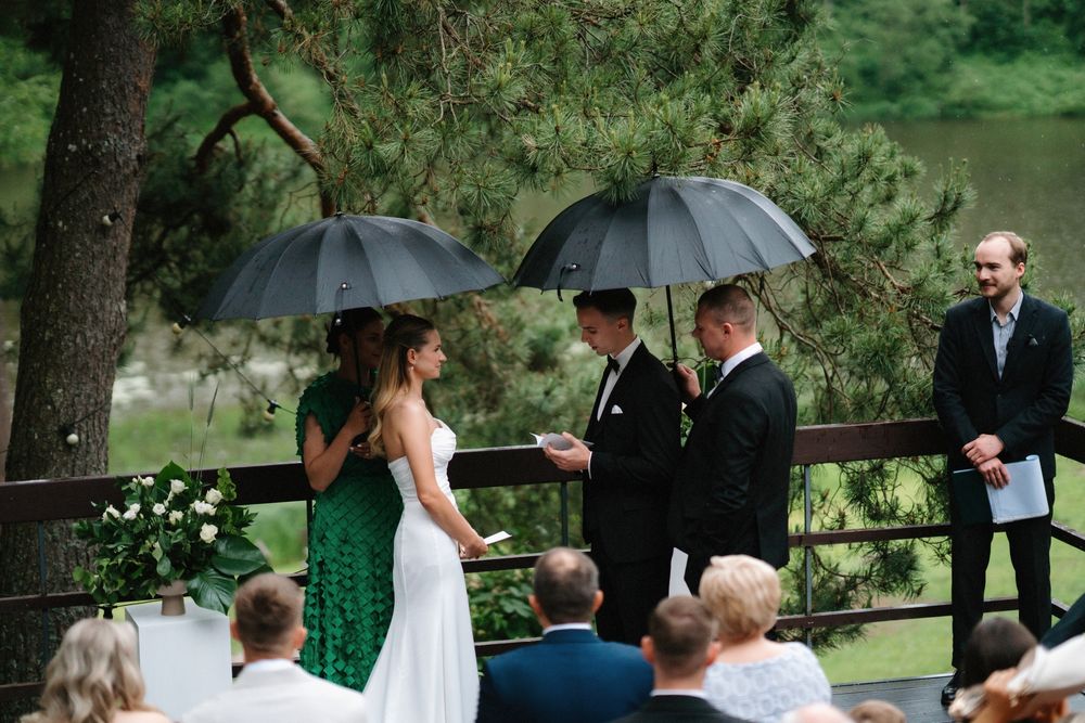 Wedding ceremony under umbrellas on a wooden deck surrounded by pine trees.