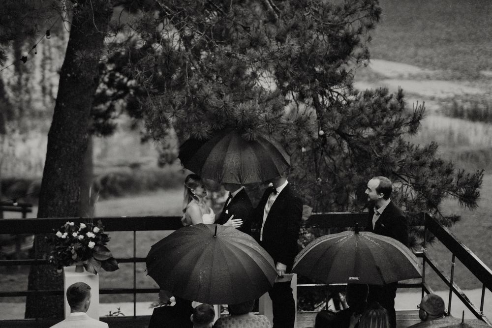 Black and white photo of a rainy wedding ceremony with umbrellas on an outdoor deck.