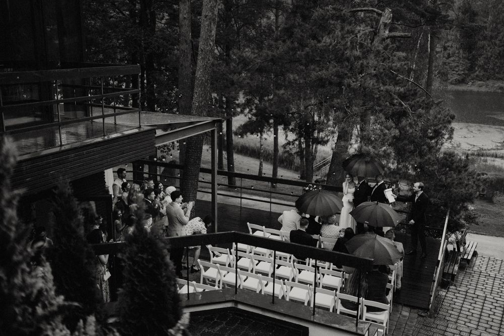 Elevated view of wedding guests seated at an outdoor ceremony space among trees.