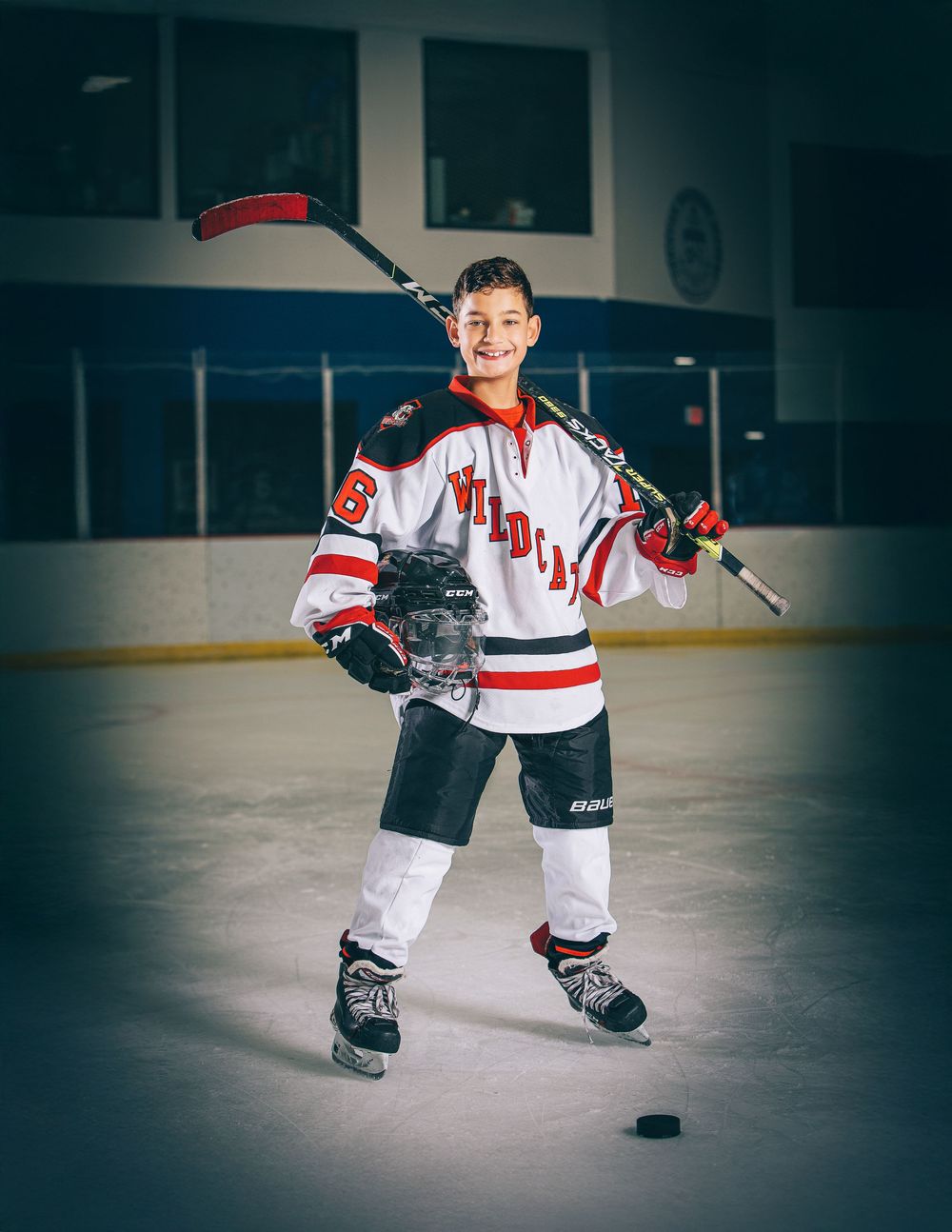 Youth hockey player in white and red jersey stands confidently on ice with stick and puck during practice session.