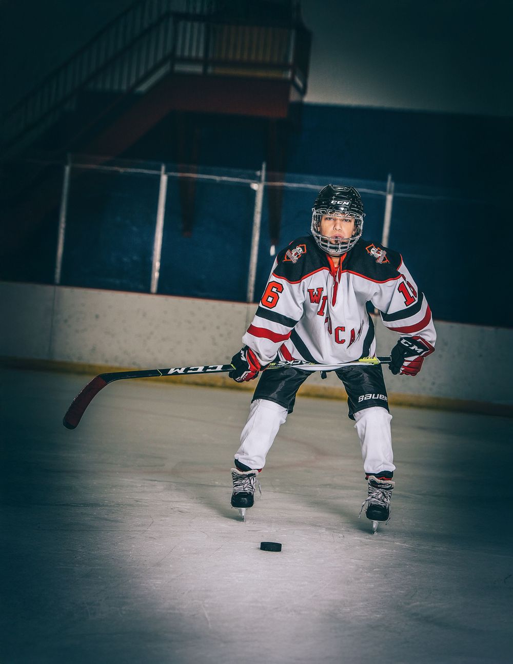 Hockey player in white jersey crouches low on ice while handling puck during game practice.