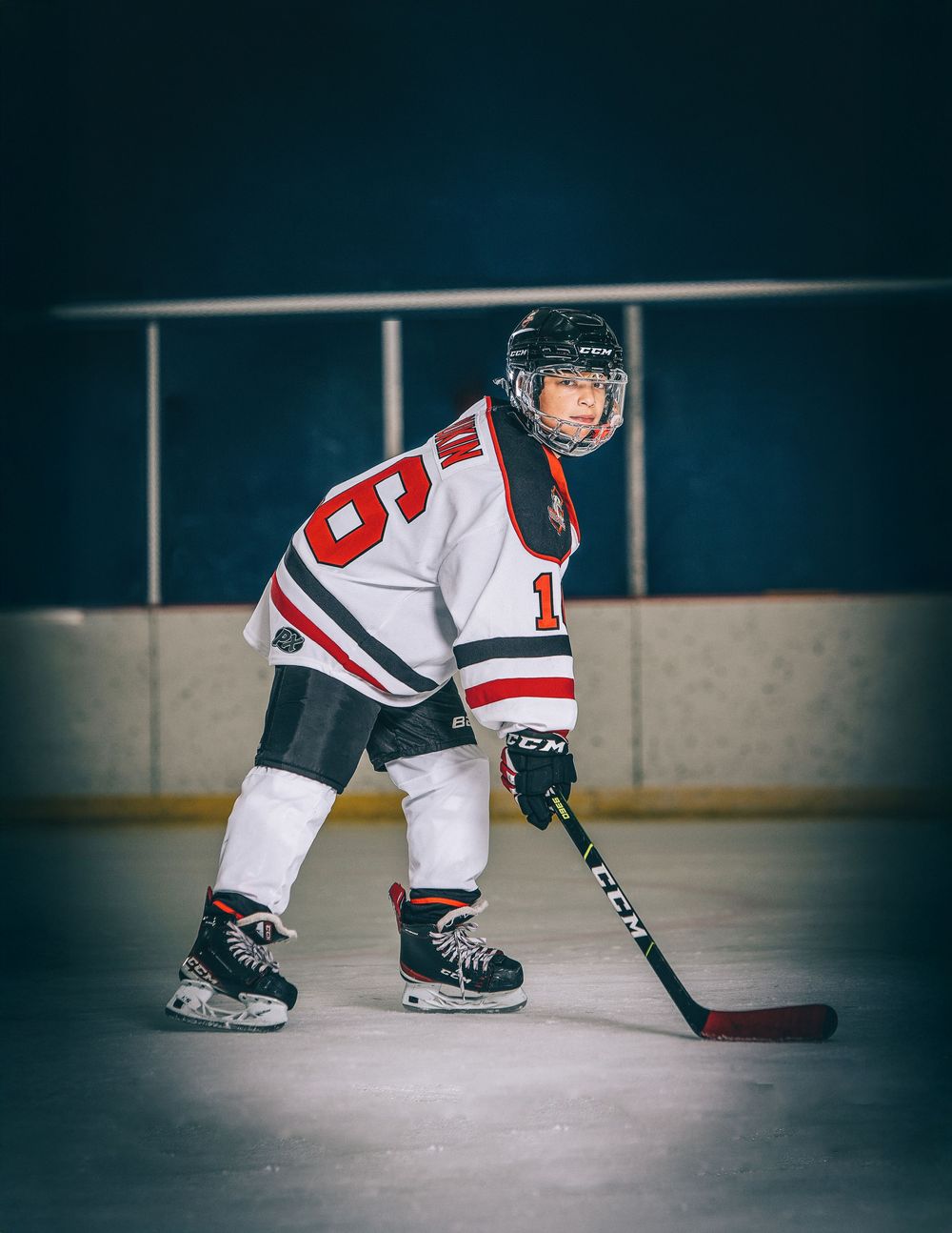 Hockey player in white jersey practicing stick handling skills on ice rink during training session.