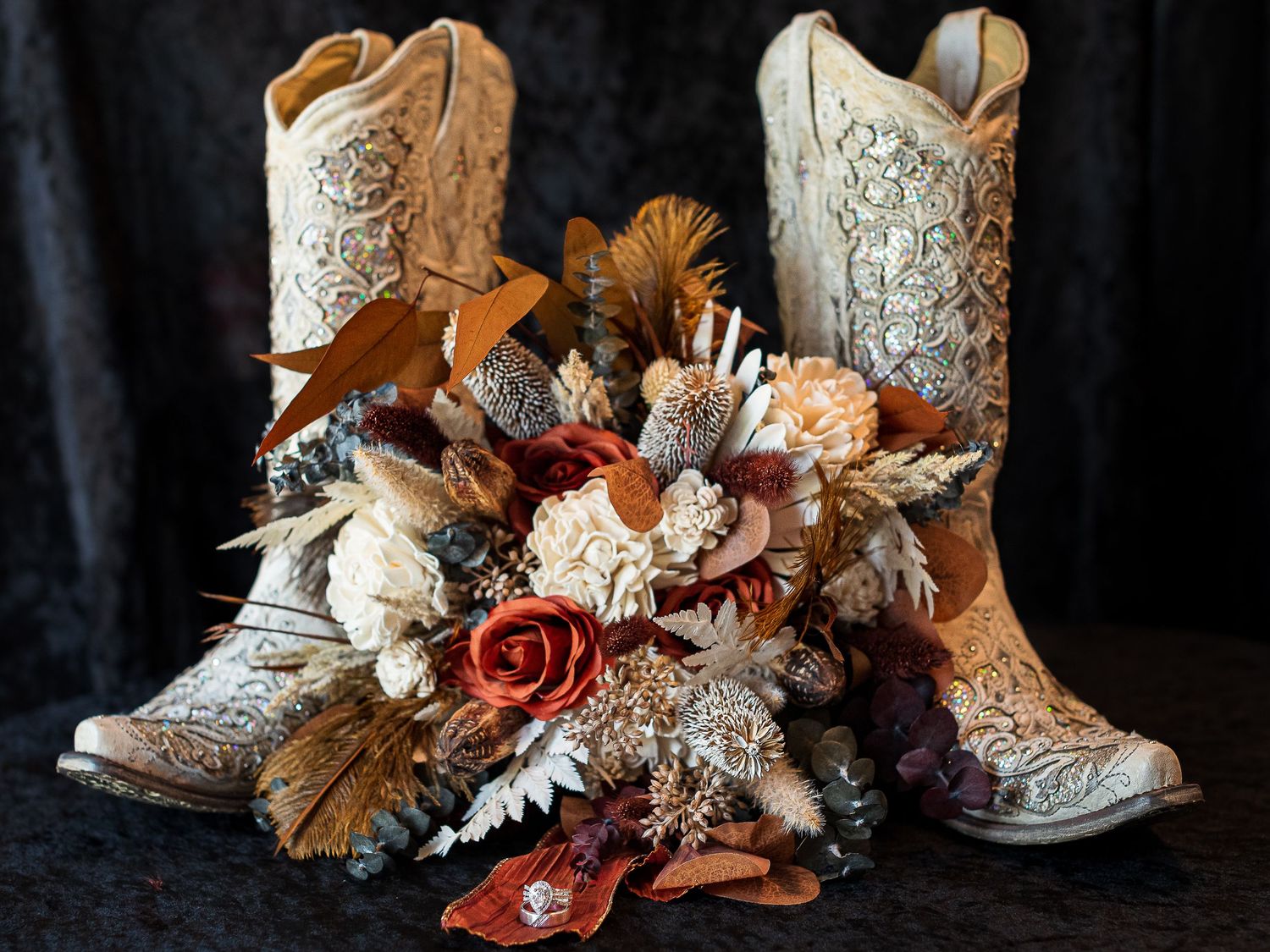 Rustic wedding boots and floral decorations arranged against a dark background.