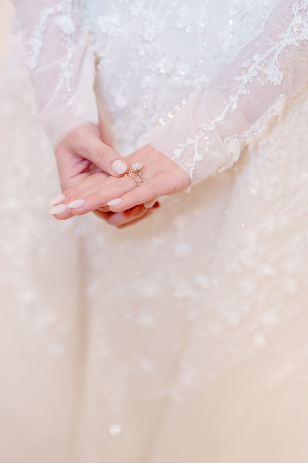 Close-up of bride's hands showing diamond engagement ring on white lace wedding dress.