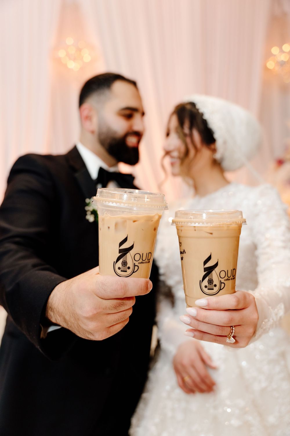 Newlyweds toast with iced coffee drinks in clear cups at their elegant wedding reception.