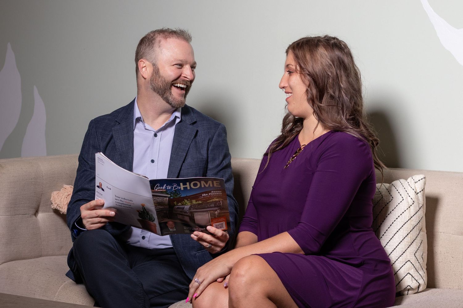 Lifestyle branding photo of two professionals chatting on a couch while looking over a magazine during a business session.