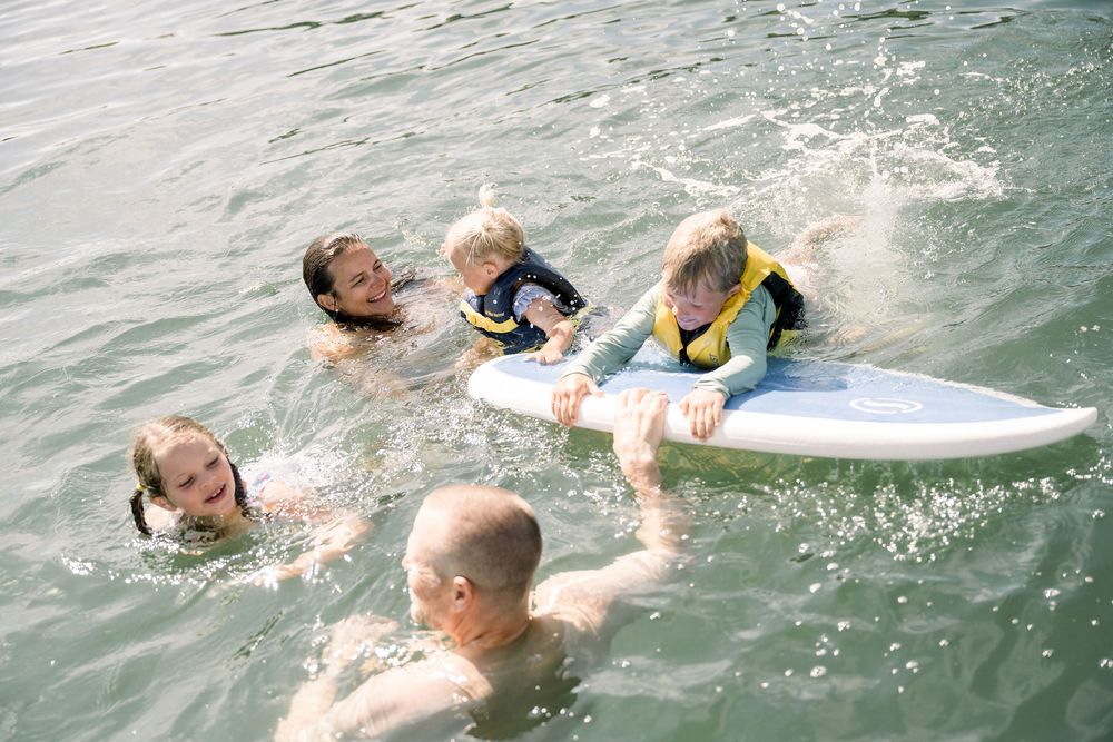 A group of swimmers enjoying a summer day in the water with surfboards and splashing around.