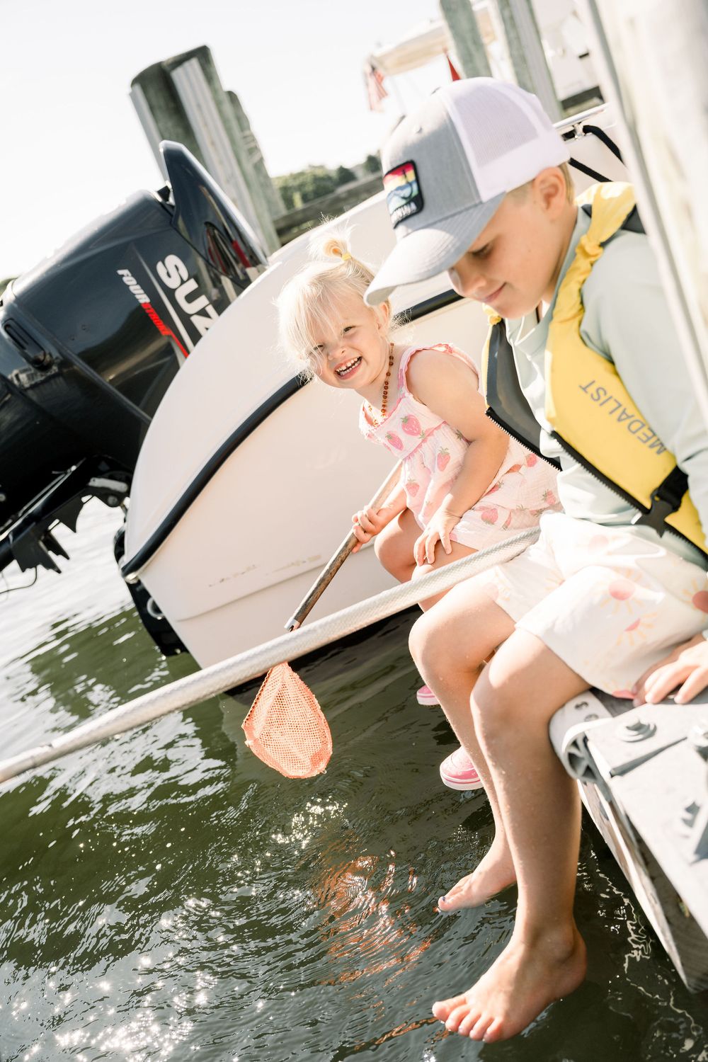 A joyful moment on a boat as a child in pink dress learns to fish with guidance on a sunny summer day.