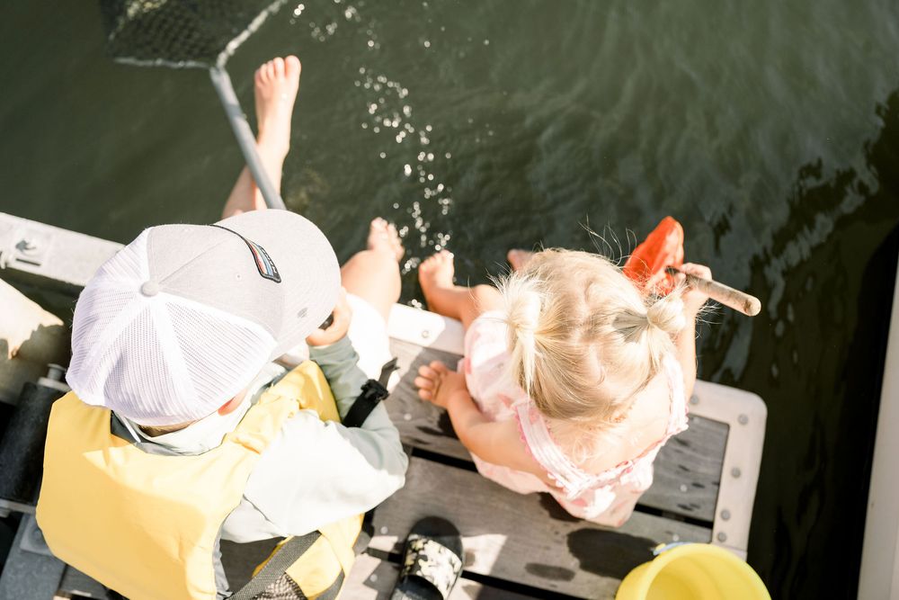 Overhead view of two people relaxing on a boat dock on a sunny summer day with feet dangling over water.
