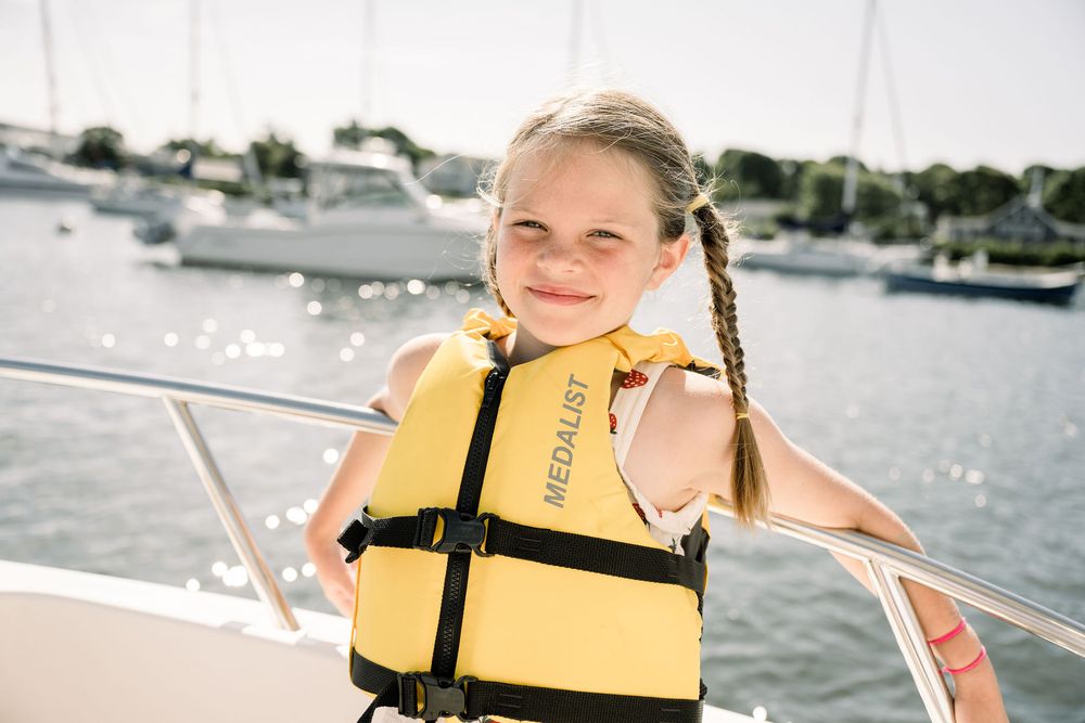 A group enjoying a sunny day sailing on a boat wearing yellow life jackets on calm waters.