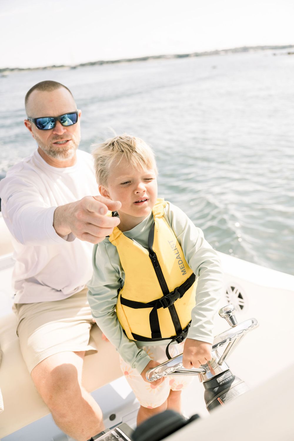 A sunny boat ride shows a person in a white shirt and another wearing a yellow life jacket on calm waters.